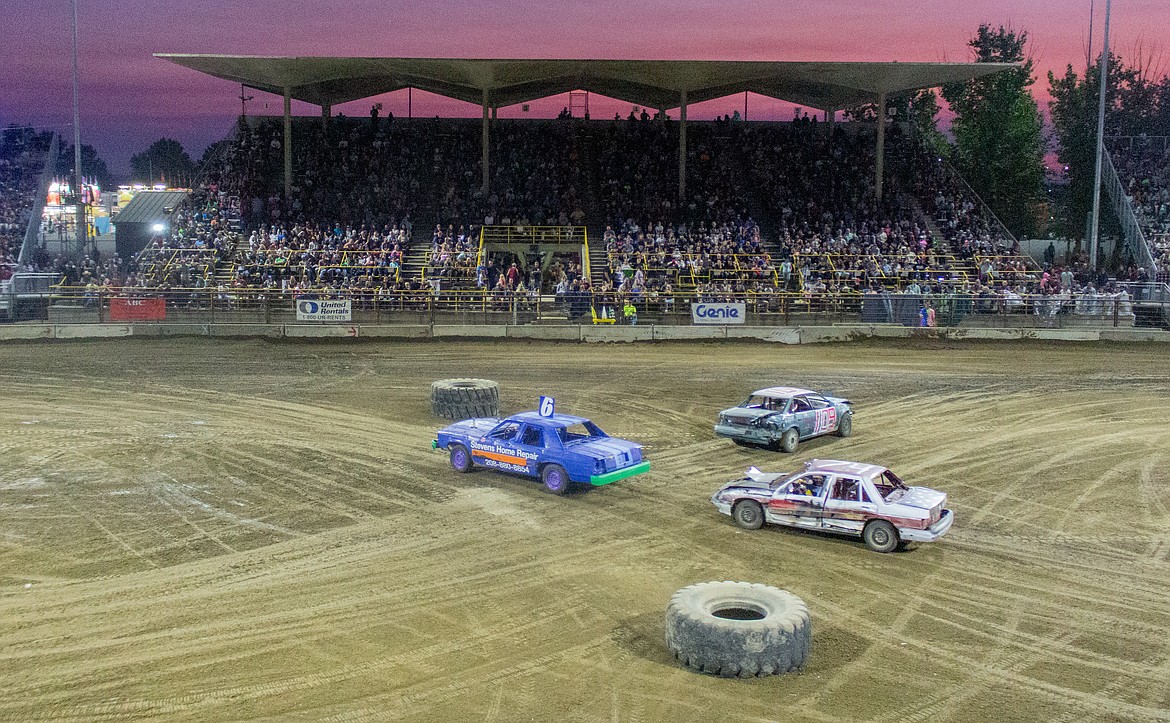 Cars cross paths in the middle of the arena during one of two Figure 8 races as the sun sets in the background Wednesday night at the Northwest Ag Demolition Derby.