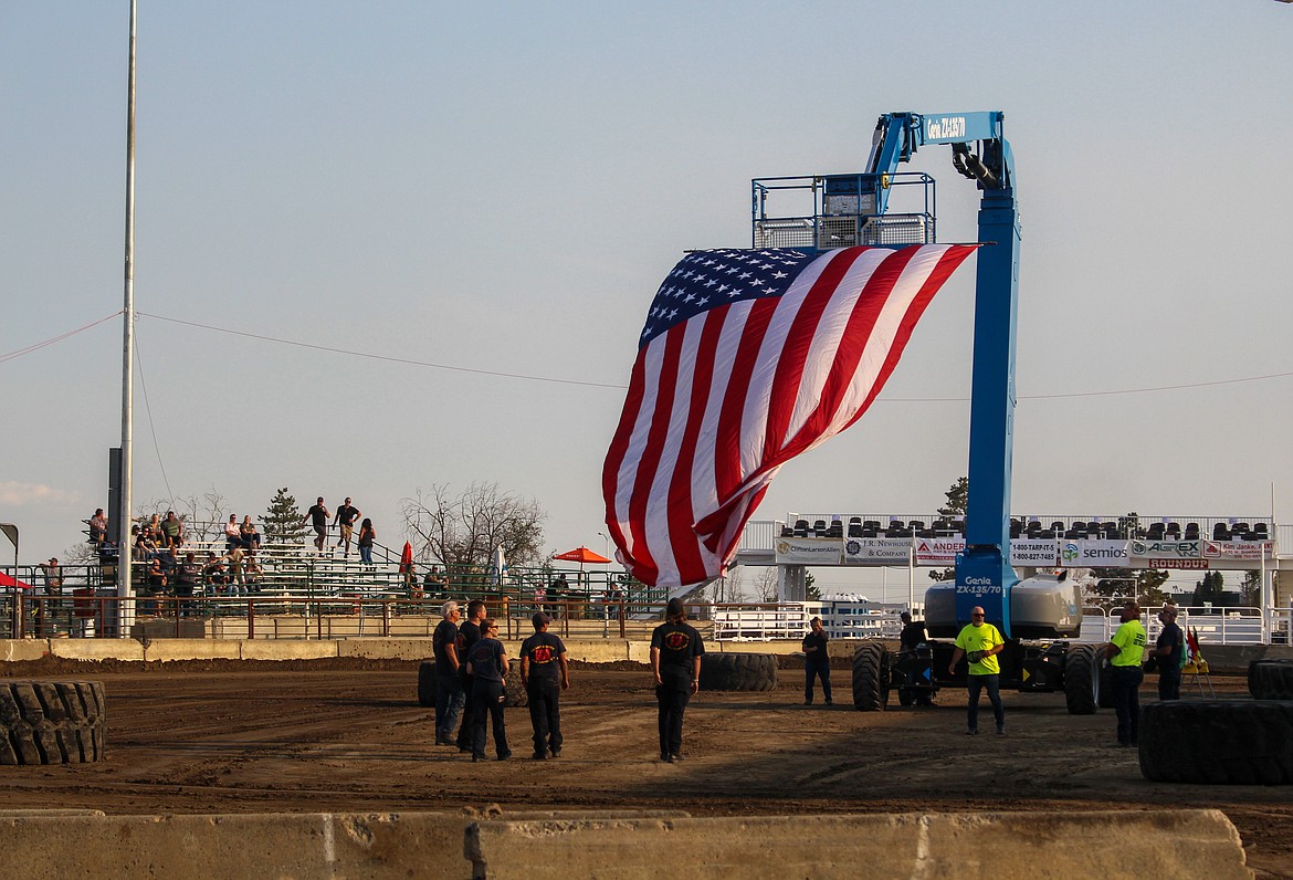 Firefighters and representatives from Genie help raise the flag in the middle of the arena before opening ceremonies Wednesday at the Northwest Ag Demolition Derby.