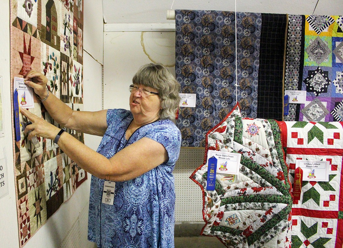 Barbara Bolton gets quilts in place at the quilt exhibit in the Home Ec Building at the Grant County Fairgrounds Tuesday morning.