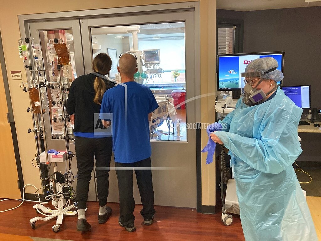 Two visitors peer into the room of a COVID-19 patient in the intensive care unit at Salem Hospital in Salem, Oregon, on Friday, Aug. 20, 2021, as a nurse dons full protective gear before going into the room of another patient. The hospitalization rate of unvaccinated COVID-19 is breaking records and squeezing hospital capacity, with several running out of room to take more patients. (AP Photo/Andrew Selsky)