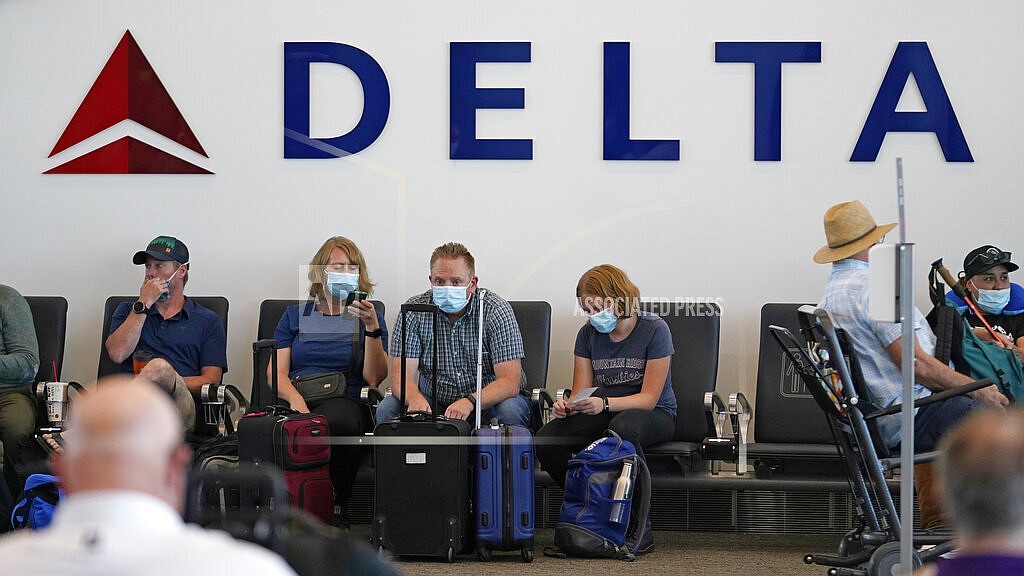 People sit under Delta sign at Salt Lake City International Airport on July 1, 2021, in Salt Lake City. Delta Air Lines won't force employees to get vaccinated, but it's going to make unvaccinated workers pay a $200 monthly charge. Delta said Wednesday, Aug. 25, 2021 that it will also require weekly testing for unvaccinated employees starting next month, although the airline says it'll pick up the cost of that testing. (AP Photo/Rick Bowmer, file)