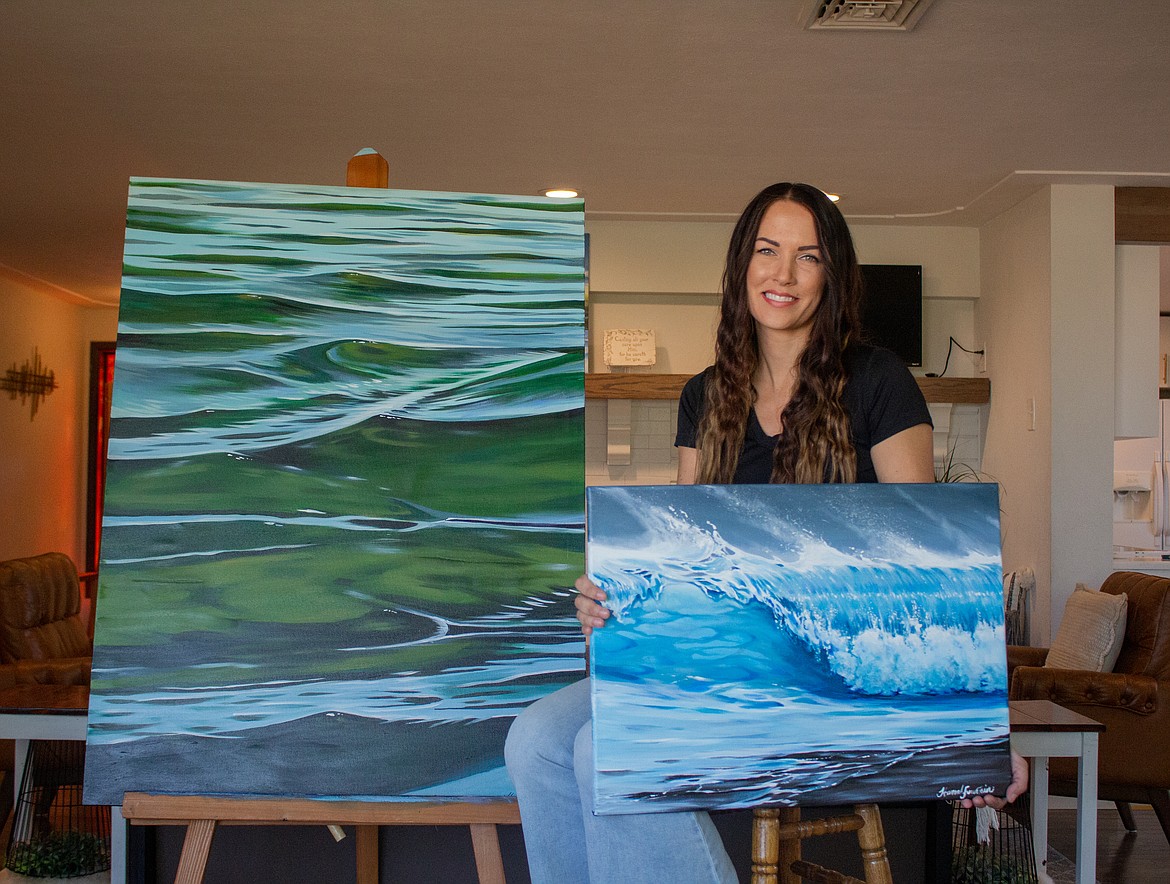 Hannah Fountain holds up one of her pieces while sitting next to another stationed on an easel in her home in Moses Lake.