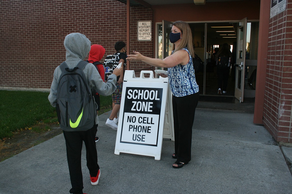 Frontier Middle School Principal Guinevere Joyce hands a mask to a student on the first day of classes Wednesday.