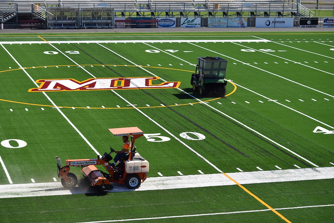 Employees with FieldTurf scatter shredded rubber and sweep sand as they prepare the new artificial turf for the first football game of the season on Saturday.