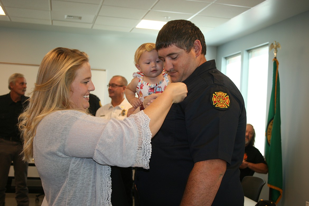 Heather Massey (left) pins the firefighters badge on her husband, a firefighter with Grant County Fire District 8, Ross Massey (right), while daughter Rylinn looks on during the dedication of the district’s new station Saturday.