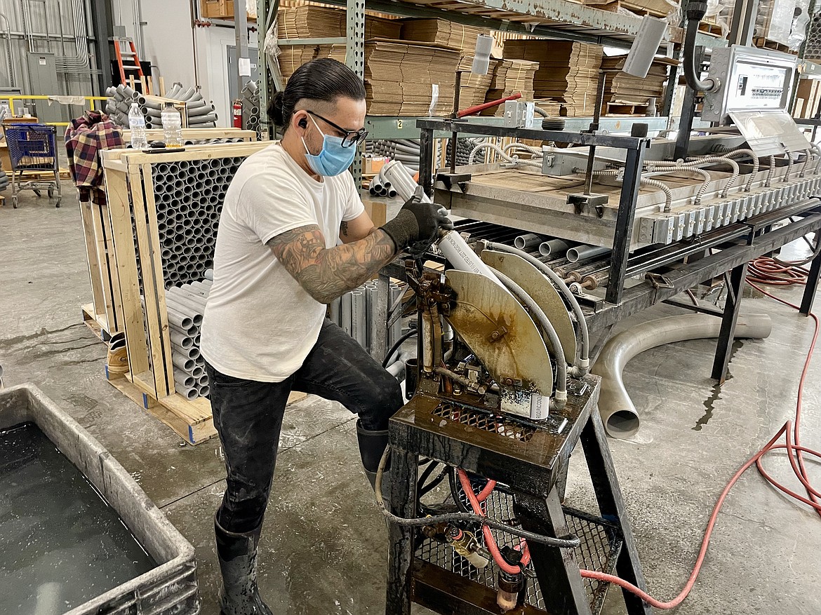 Raceways Technology employee George Mendoza bends a PVC pipe to create an elbow at the facility in Quincy. Behind him is one of the long, flat ovens where the pipe is heated so it can be pliable enough to bend.