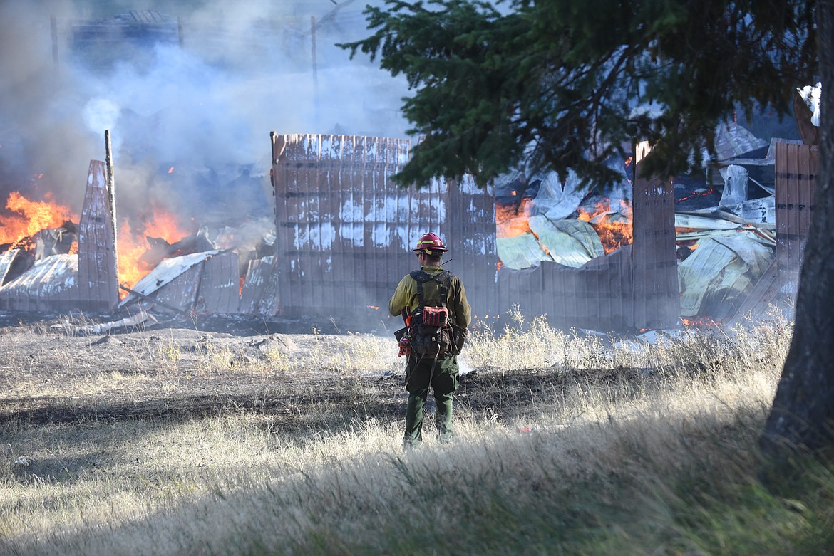 A Montana Department of Natural Resources and Conservation firefighter monitors a barn fire on Batavia Lane, west of Kalispell, Thursday afternoon. Officials said the metal structure was used as a shop and no animals were inside the building. The cause of the fire has yet to be determined. Fire crews from Smith Valley, West Valley, South Kalispell and Kalispell responded. Flathead County Sheriff's officers worked traffic control. (Scott Shindledecker/Daily Inter Lake)