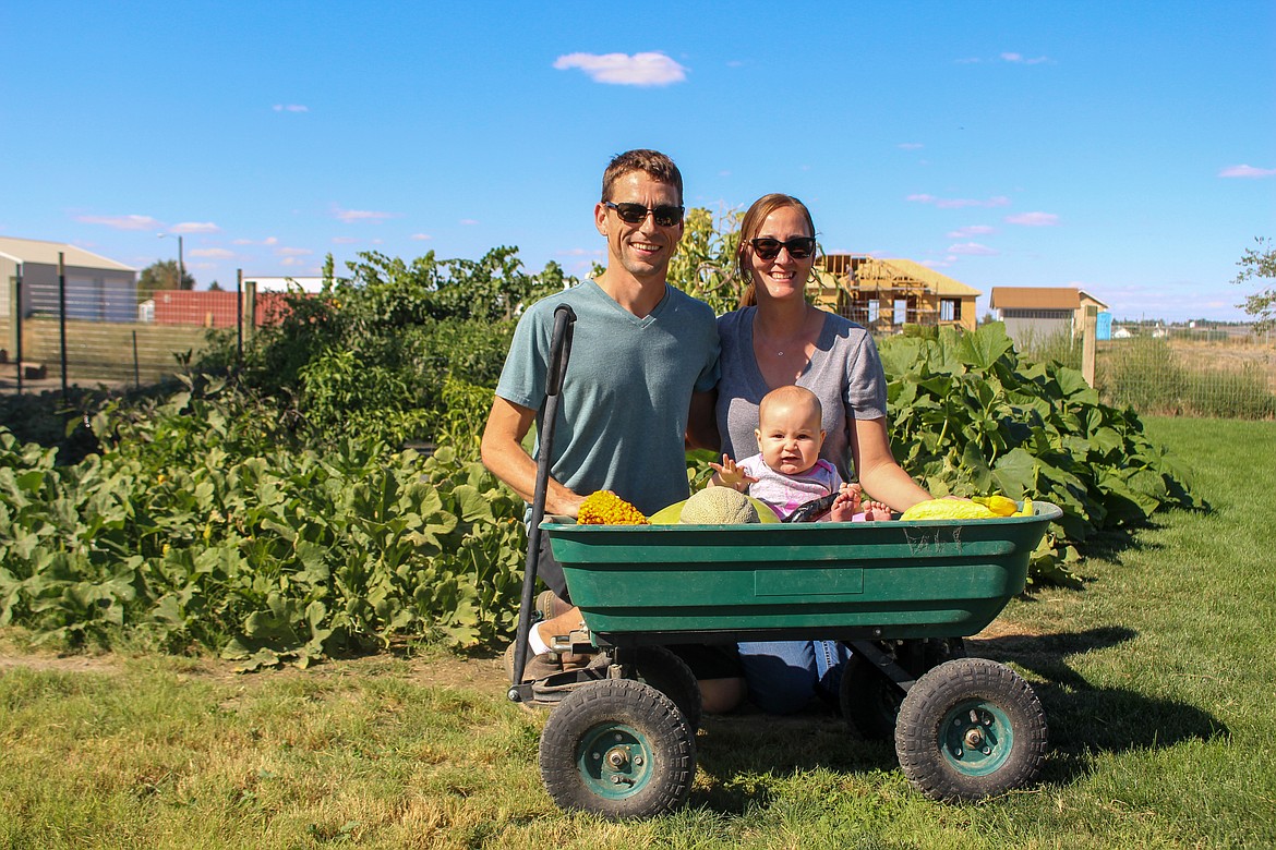 Darrel Jensen, Lacey Jensen and their daughter Mae Jensen sit in front of their garden with a wagon full of fresh produce on Sept. 1 outside of Moses Lake.