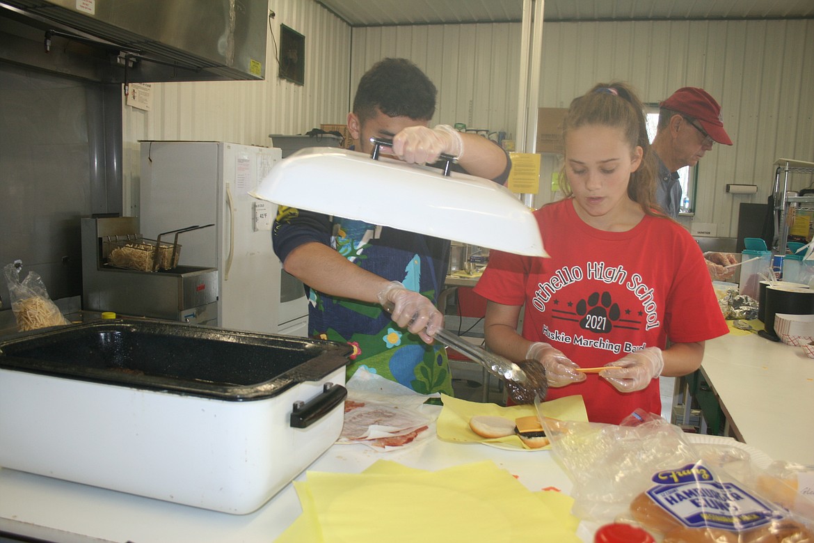 Noah Garza (left) and Macey Lutey (right) put together a hamburger at the 4-H booth Saturday. Othello High School band students volunteered at the booth to raise money for band activities.