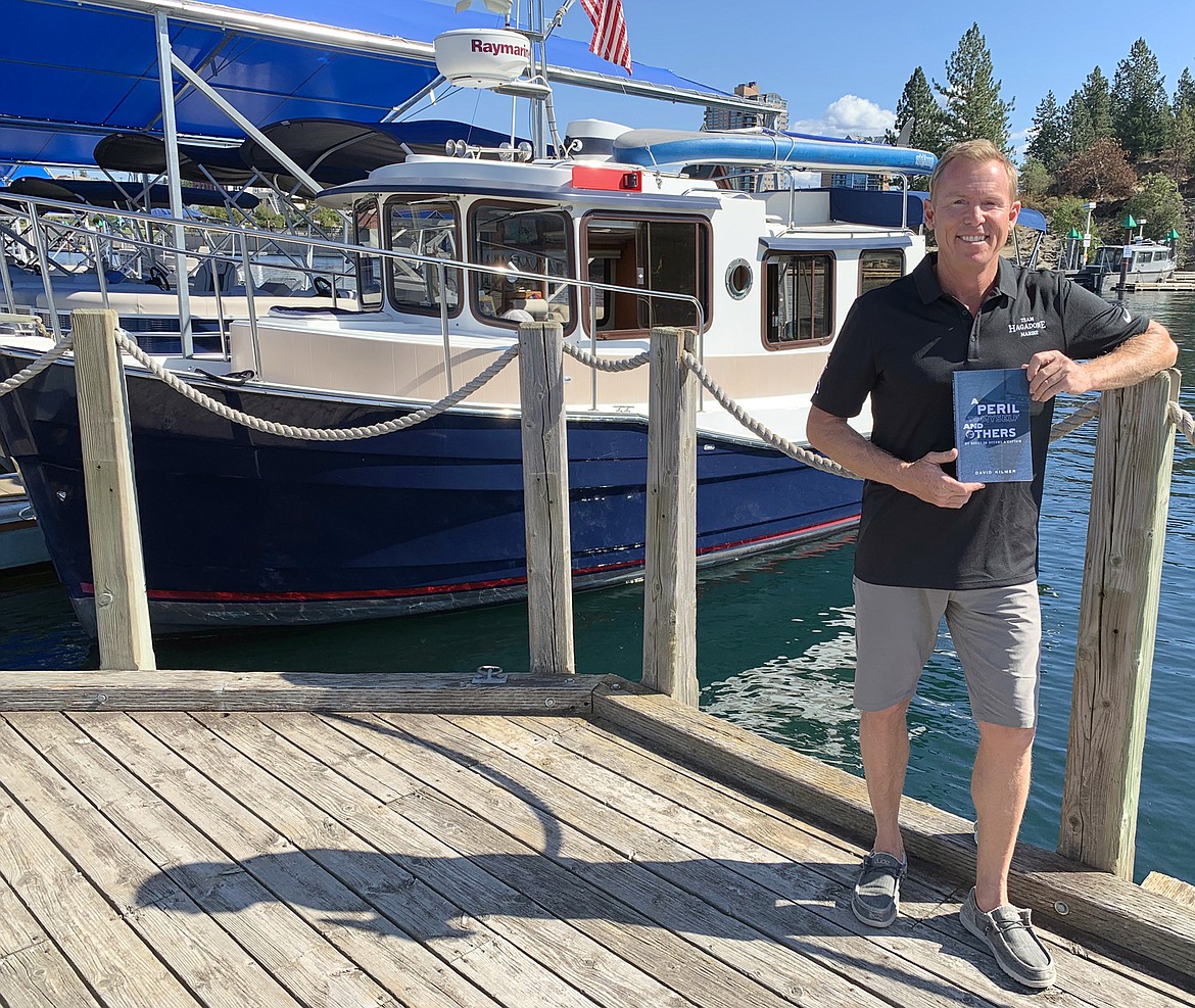 David Kilmer holds a copy of his new book and stands in front of his 27-foot tugboat at the Boardwalk Marina.
