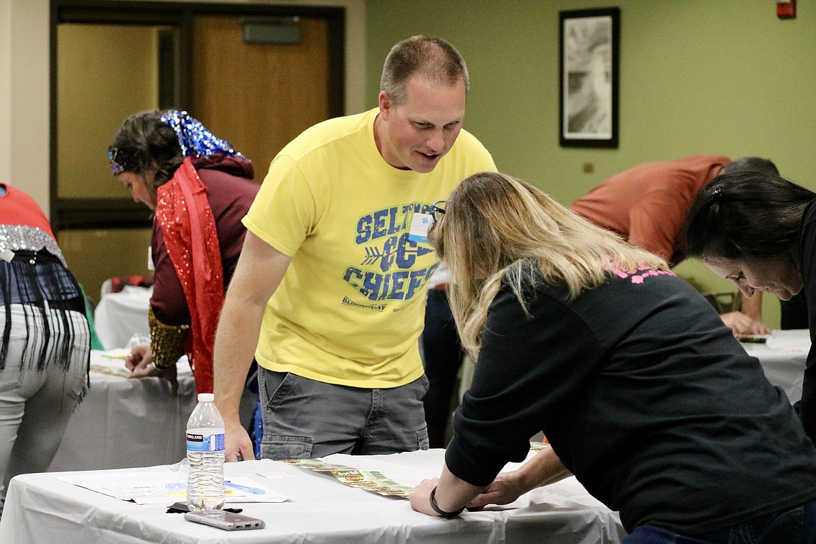 Tim Rice, a PE teacher at Seltice Elementary School, helps his teammates get their tickets scratched at the 21st annual Scratch for Schools on Thursday evening at North Idaho College. HANNAH NEFF/Press