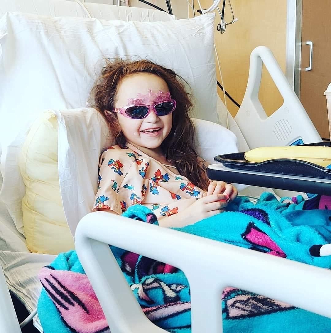 Harmony Rowe smiles from her hospital bed, rocking a pair of pink sunglasses with a tiara along the top of the frame.