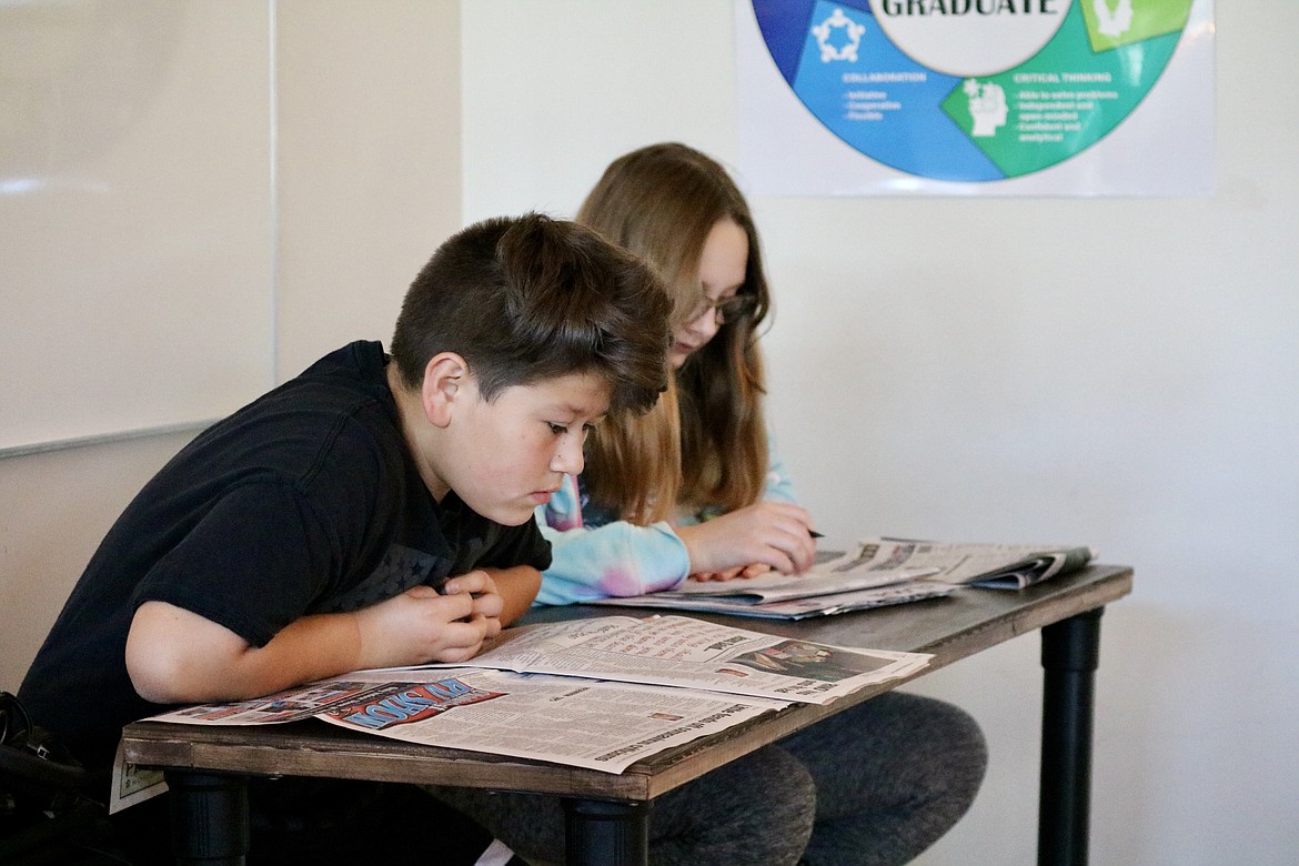 Owen Derri and Ember Pederson read through copies of The Coeur d'Alene Press to find articles that interest them to write about in history class at Lakes Middle School. HANNAH NEFF/Press