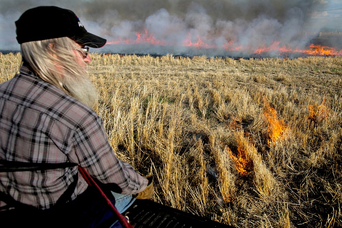 In this Oct. 22, 2015, file photo, Don L. Butler sits on the tailgate of a pickup truck as he lights a wheat field on fire using a wheat burning torch to help the field recycle its crops near the intersection of Greensferry Road and Hayden Avenue north of Post Falls.