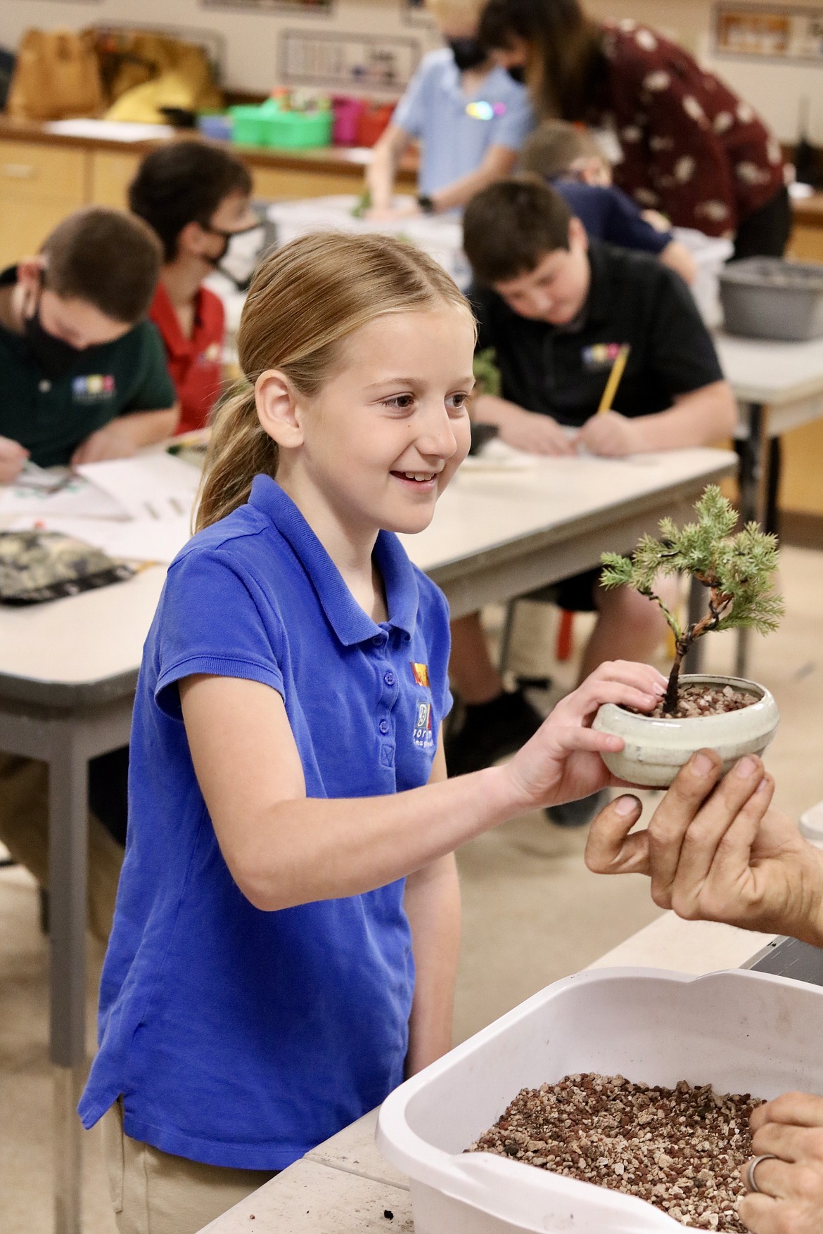 Fifth-grader Miriam Pratt smiles as she takes her newly potted bonsai tree to the next station to apply the rock ground cover on Thursday at Sorensen Magnet School of the Arts and Humanities in Coeur d’Alene. HANNAH NEFF/Press