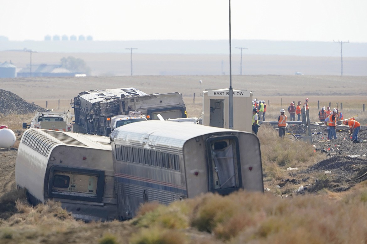 In this Sept. 27, 2021, file photo, workers stand near train tracks next to overturned cars from an Amtrak train that derailed near Joplin, Mont. A preliminary report released Tuesday, Oct. 16, 2021, on the derailment of an Amtrak train in north-central Montana last month that killed three people and injured dozens more gave no information on the cause of the accident. (AP Photo/Ted S. Warren, File)