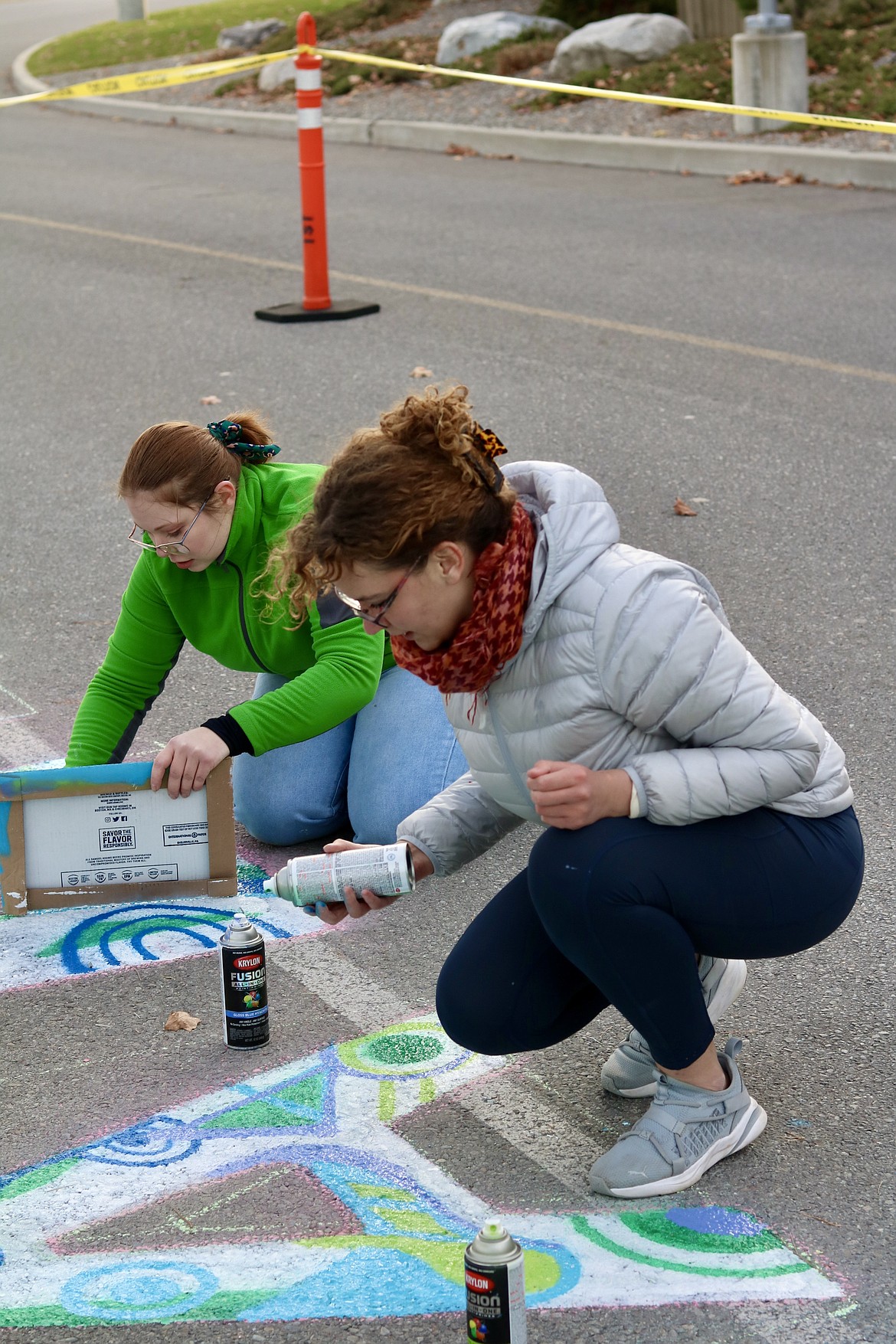 From left, 19-year-old North Idaho College student artists Grace Michelsen and Annie Vladovska, the student government president and creator of the graffiti design, spray paint a thank you message to health care workers on the pavement on Kootenai Health Way on the east side of the hospital through a collaboration between Kootenai Health and NIC. HANNAH NEFF/Press