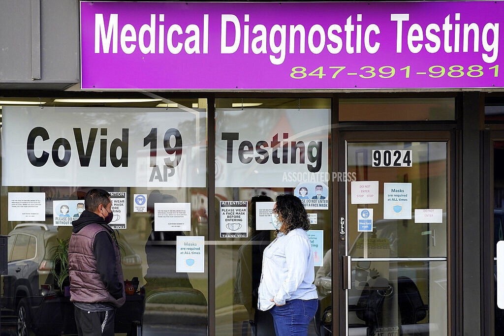 In this Oct. 21, 2020, file photo, an Exam Corp Lab employee, right, wears a mask as she talks with a patient lined up for COVID-19 testing in Niles, Ill. Millions of U.S. workers now have a Jan. 4 deadline to get a COVID vaccine. The federal government on Thursday, Nov. 4, 2021 announced new vaccine requirements for workers at companies with more than 100 employees as well as workers at health care facilities that treat Medicare and Medicaid patients. (AP Photo/Nam Y. Huh, File)