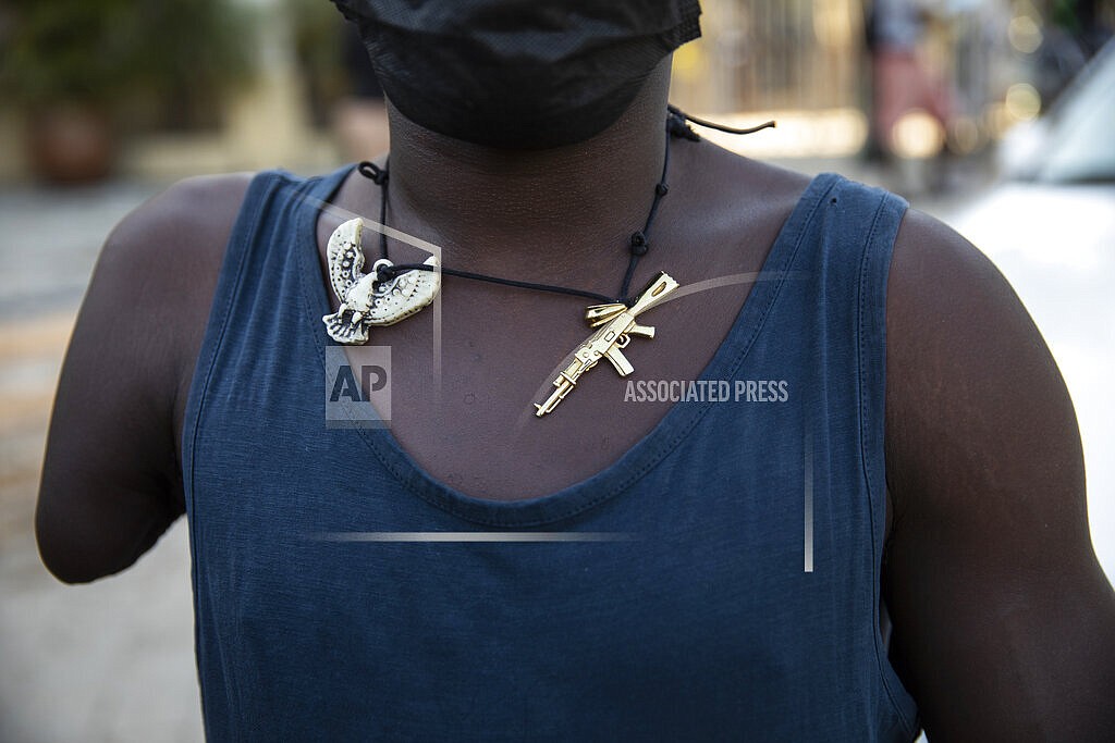 A man wearing a necklace adorned with charms depicting a phoenix and a machine gun, waits for faithful to exit the Saint Peter's Catholic church to beg for alms, in Port-au-Prince, Haiti, Tuesday, Sept. 28, 2021. (AP Photo/Rodrigo Abd)