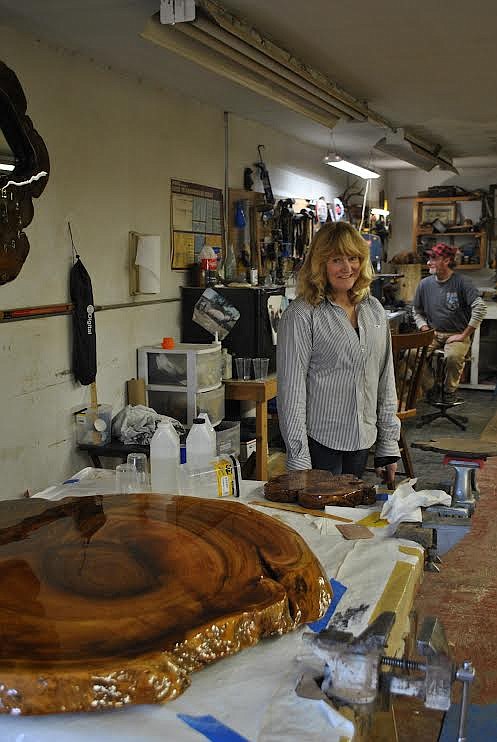 Kim Elledge stands in her woodworking shop in St. Regis, behind her is Carl, her fiancé. Together they're currently working on a huge burl slab table, the beautiful wood cut has been sealed with several coats of resin and will be attached to a root wad for its legs. (Amy Quinlivan/Mineral Independent)