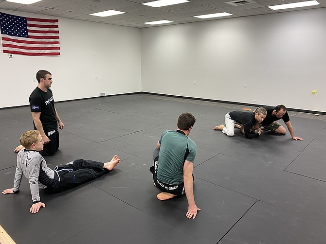 Sparta Training Academy CDA co-owner Devin Rourke, white pants, demonstrates Brazilian jiu-jitsu techniques to a class.