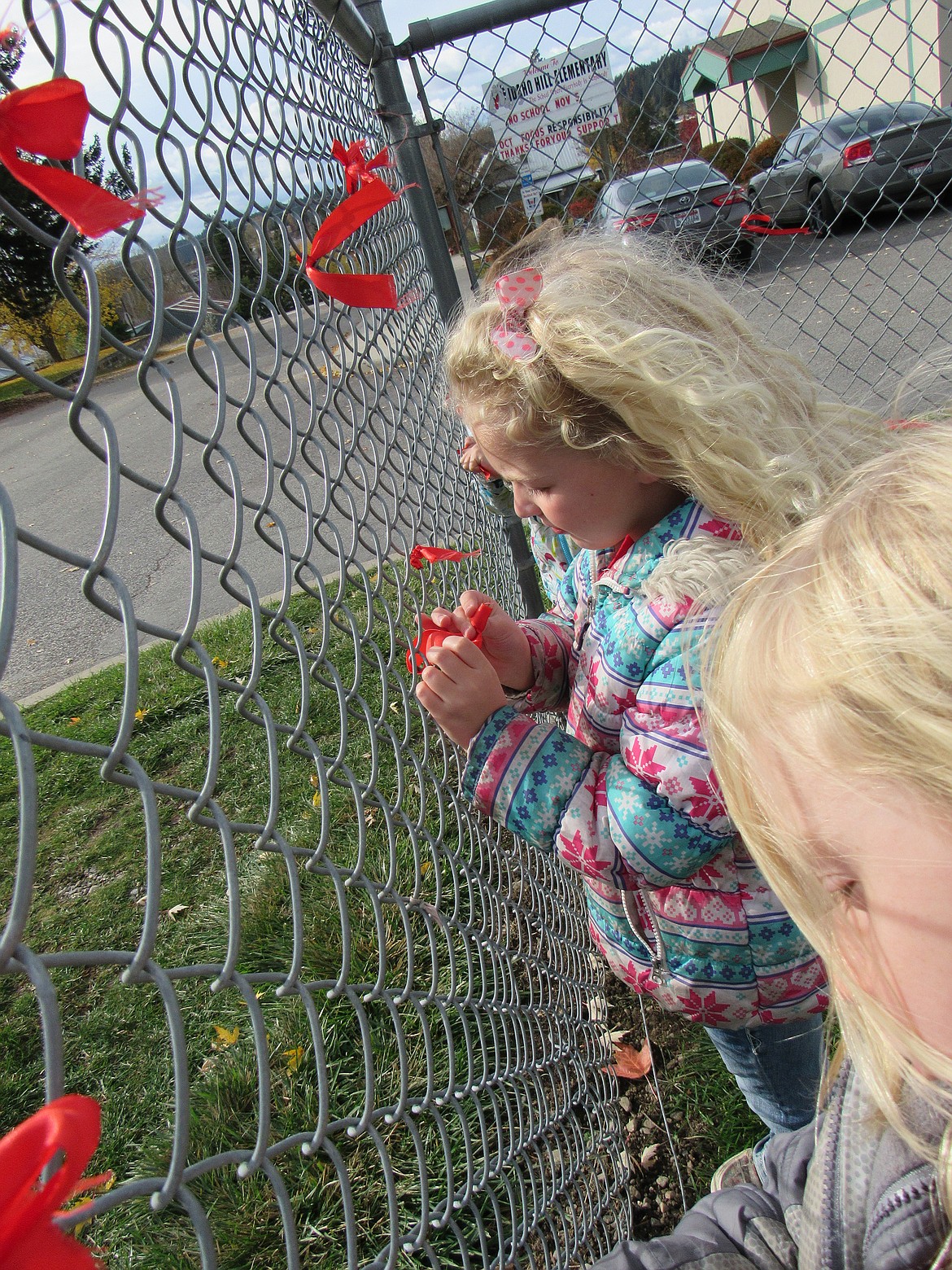 A student weaves a red ribbon into the chain-link fence outside Idaho Hill Elementary in late October in celebration of Red Ribbon Week.