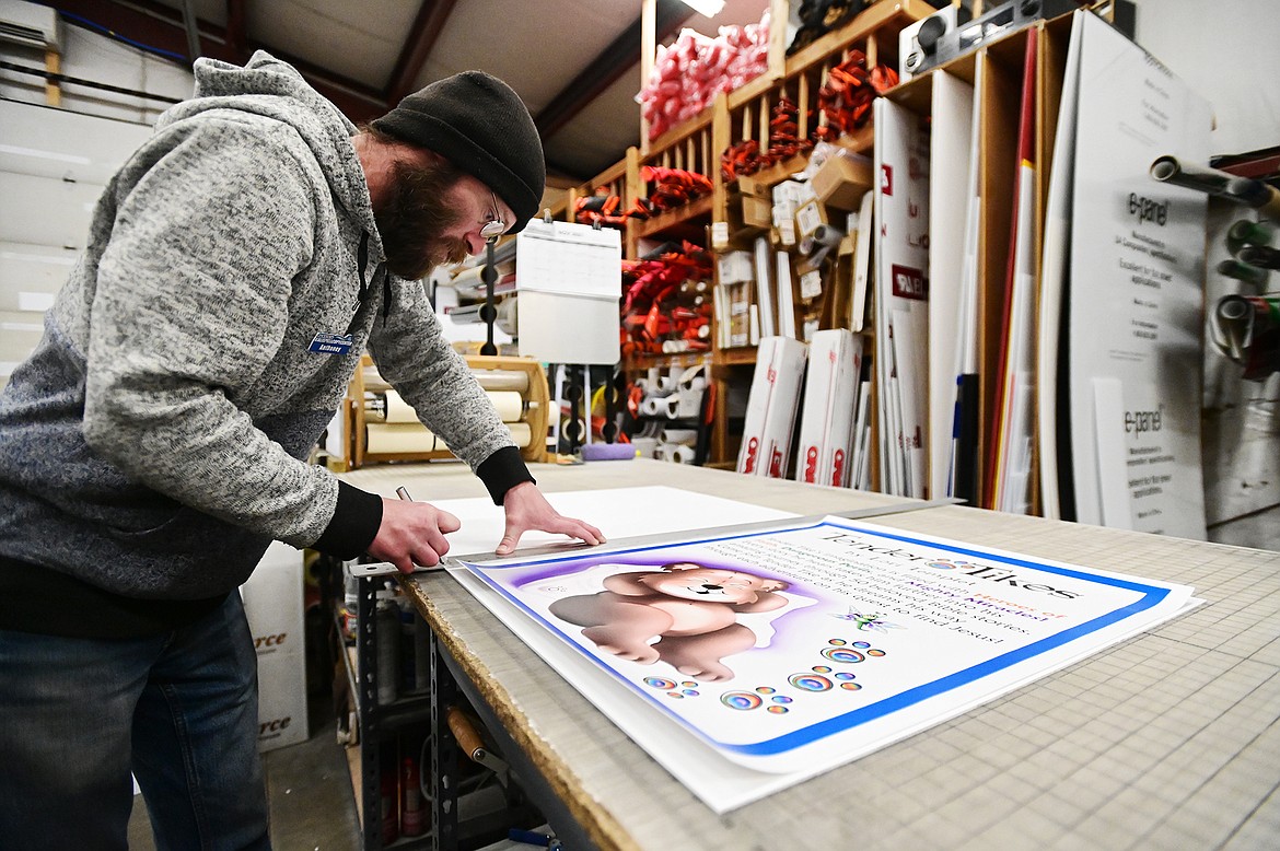 Anthoney Zollman mounts a vinyl print onto PVC plastic for a client at Kalispell Copy Center on Thursday, Nov. 11. (Casey Kreider/Daily Inter Lake)