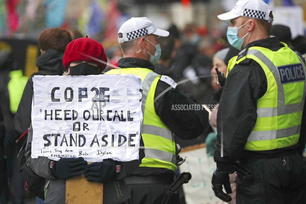 A climate activist holds a placard next to police officers near the venue for the COP26 U.N. Climate Summit in Glasgow, Scotland, Friday, Nov. 12, 2021. (AP Photo/Scott Heppell)