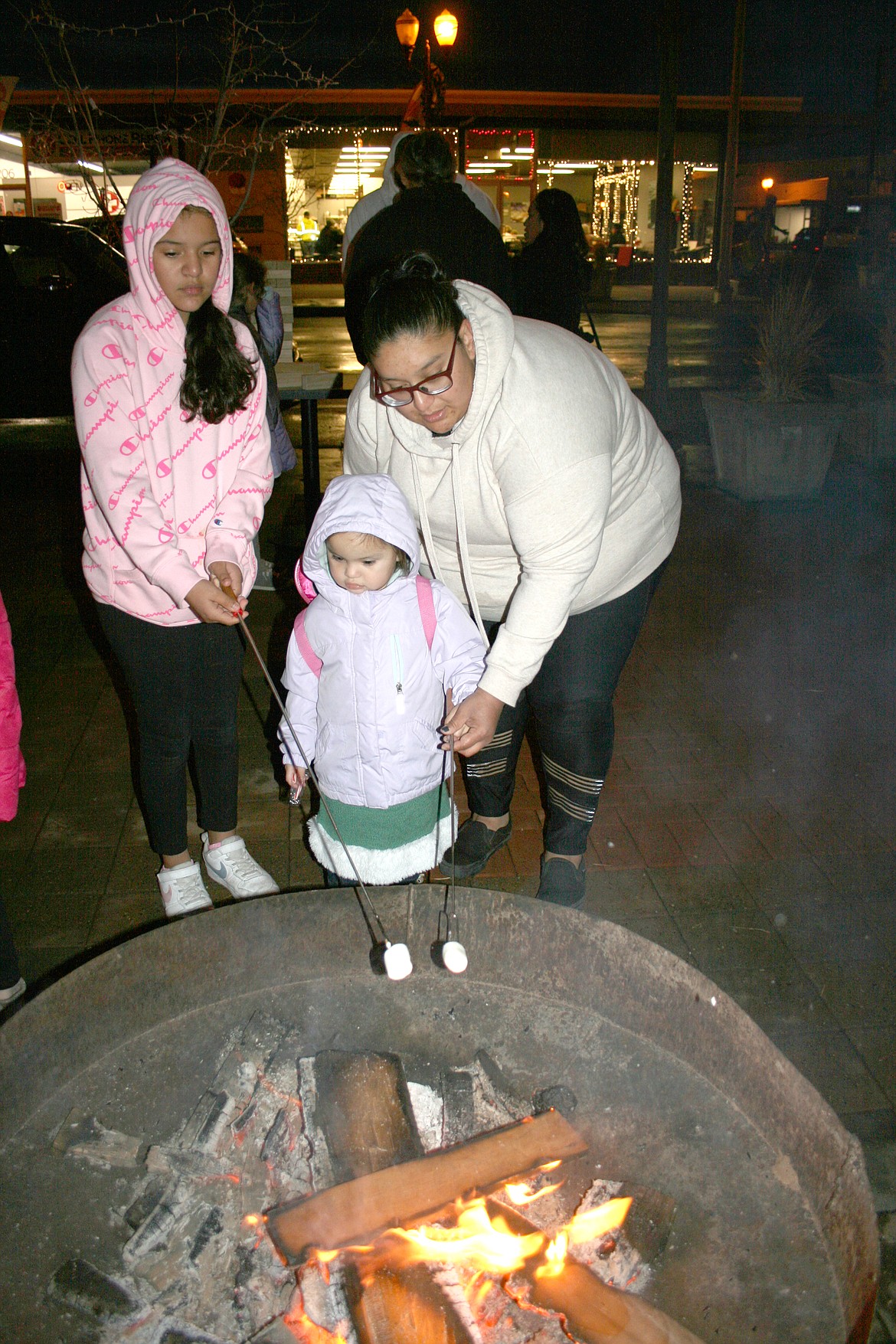 Nuriah Mendoza (center) gets help from her mom Anna Mendoza (right) to roast a marshmallow during the Downtown Moses Lake Association’s Downtown Street Tree Lighting and Holiday Open House. Sammy Mendoza is at left.