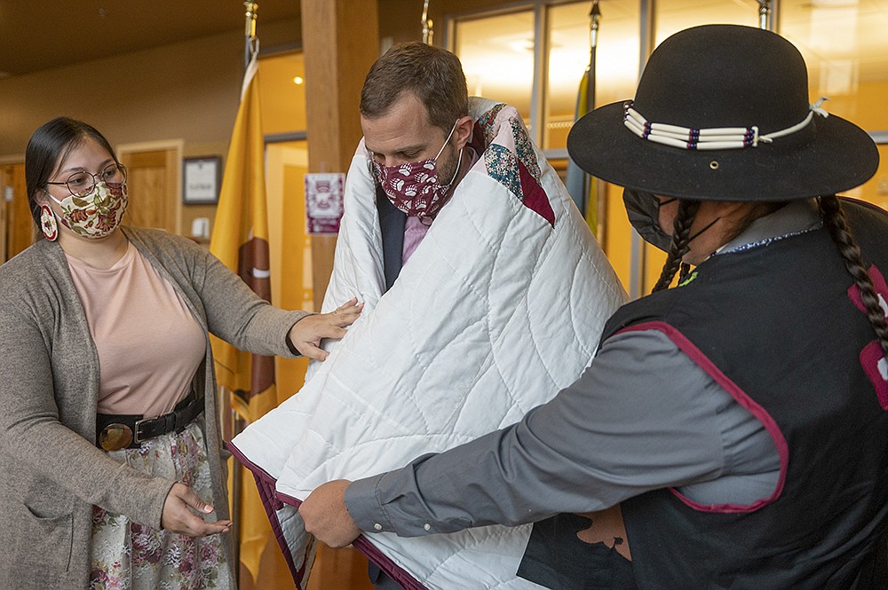 UM Kyiyo Student Club President Zachariah Rides At the Door and Kyiyo Vice President Seirra Paske present UM President Seth Bodnar with a blanket in UM's Payne Family Native American Center. (UM News Service)