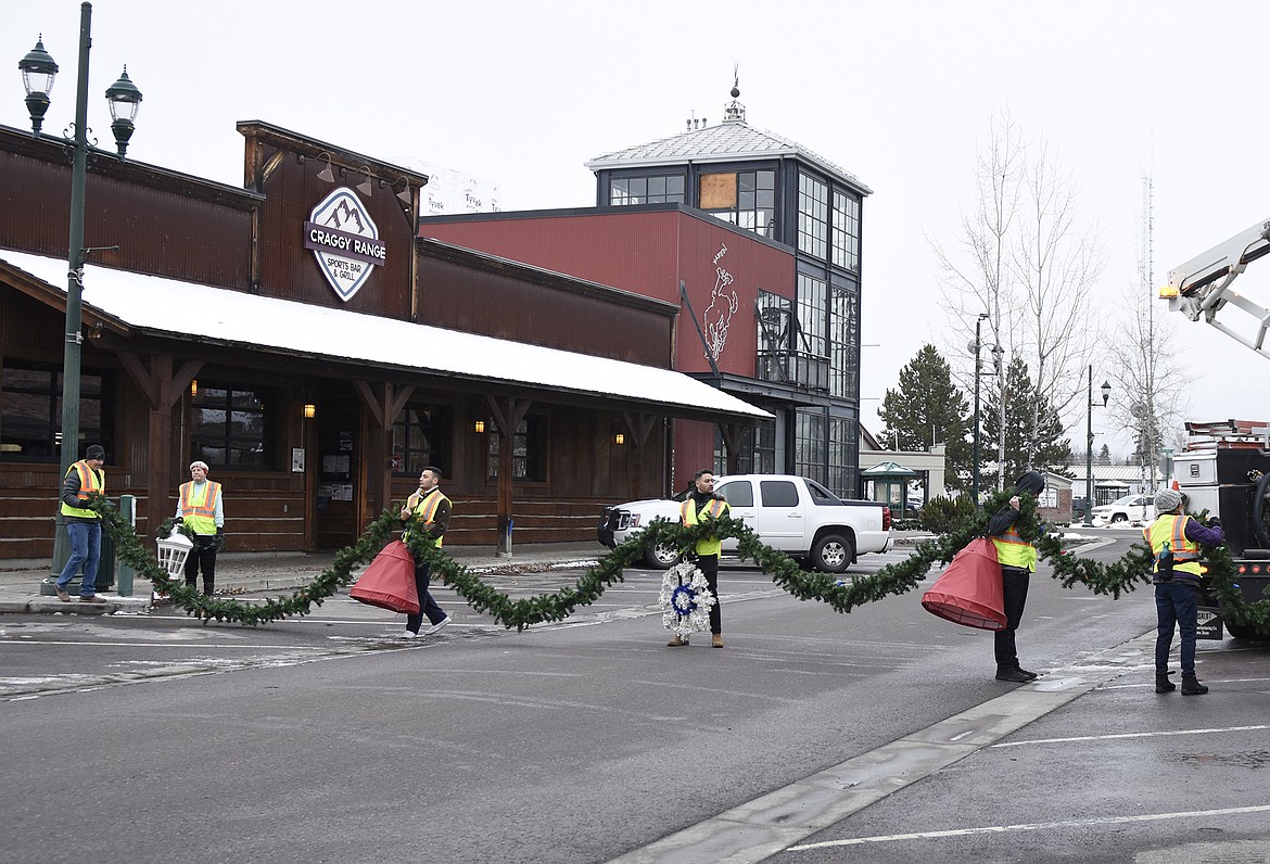 Volunteers hang the winter decorations downtown Sunday morning. (Heidi Desch/Whitefish Pilot)