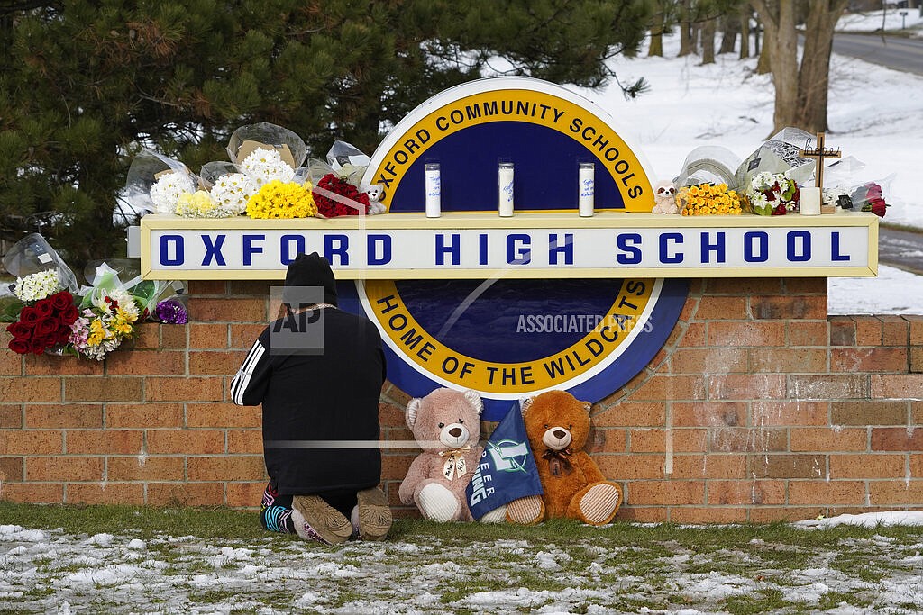 A well wisher kneels to pray at a memorial on the sign of Oxford High School in Oxford, Mich., Wednesday, Dec. 1, 2021. A 15-year-old sophomore opened fire at the school, killing several students and wounding multiple other people, including a teacher. (AP Photo/Paul Sancya)