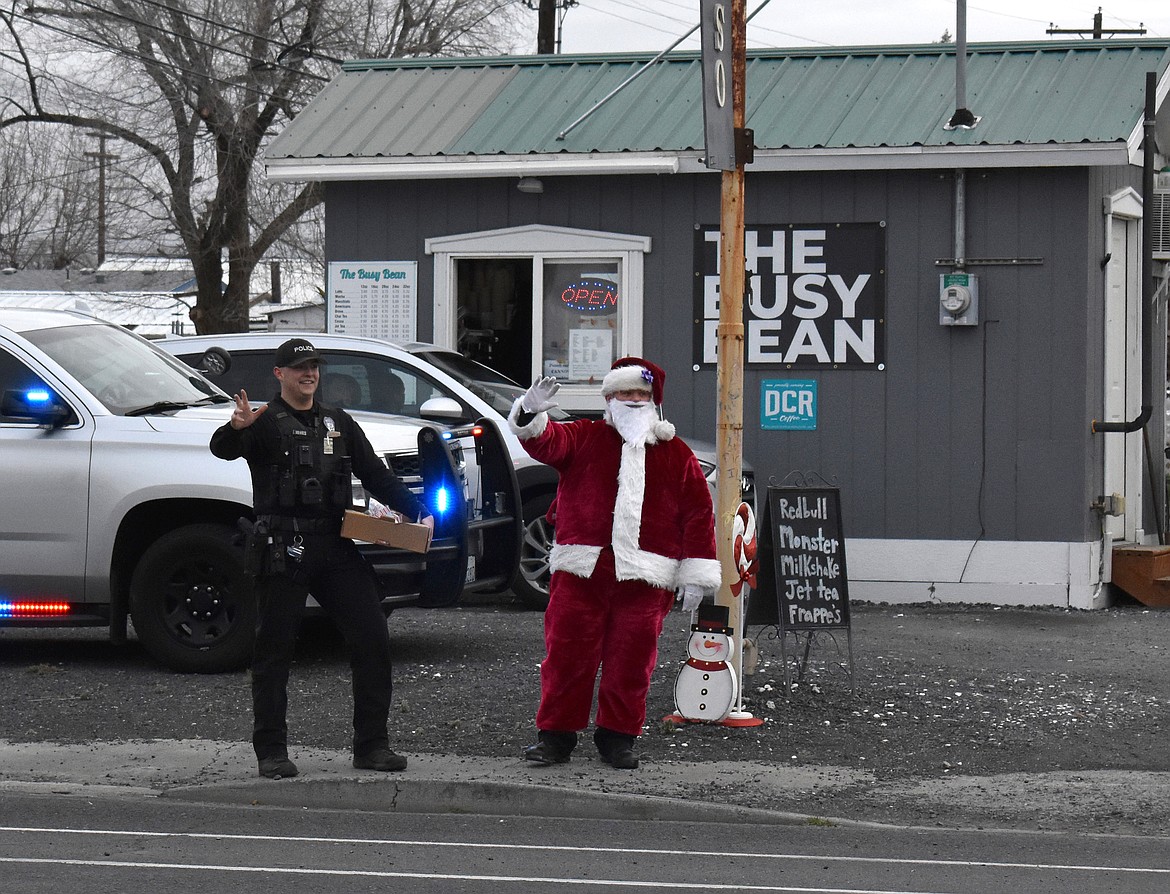 Soap Lake Police Department officers Trevor Jones, left, and Justin Rowland, in the Santa suit, wave at cars as they pass by the Tip-a-Cop event Monday.