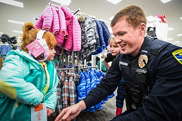 Columbia Falls Police patrolman Wayne Stufflebeem helps a young girl zip up a coat during the Shop With A Cop program at Target in Kalispell on Wednesday, Dec. 8. (Casey Kreider/Daily Inter Lake)