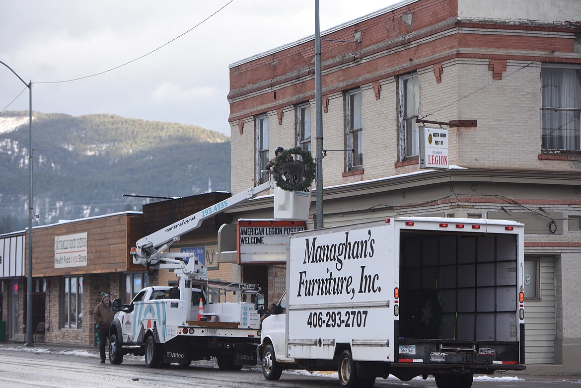 A Montana Sky employee hooks a Christmas wreath up to a light pole on California Avenue on Wednesday, Dec. 8, 2021. (Derrick Perkins/The Western News)