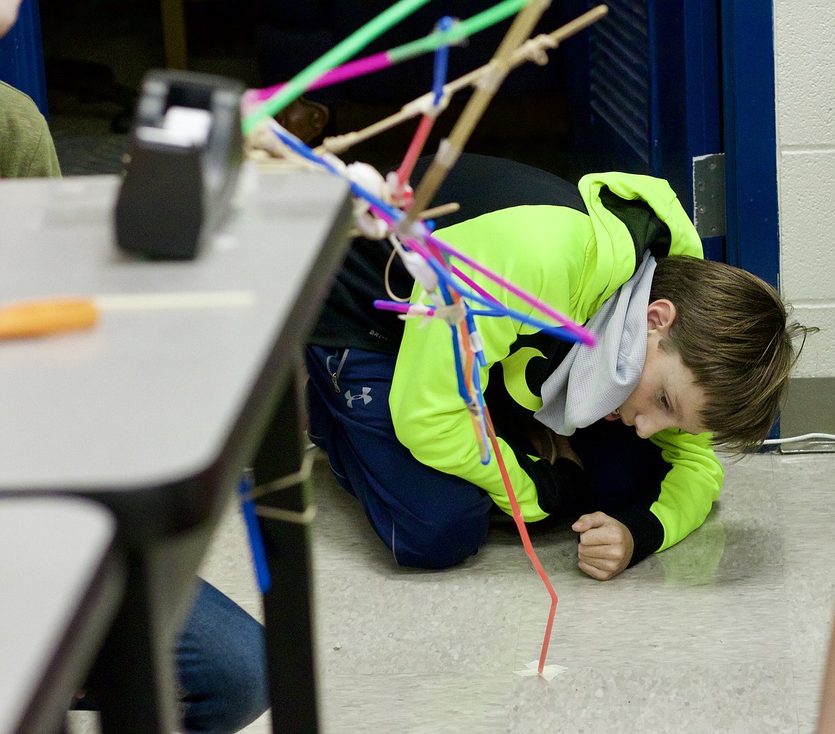 Seventh grader Wyatt Hartzell checks on his team's cantilever, a bridge with only one contact point, to make sure it isn't touching the floor. The students used supplies like spoons, straws, popsicle sticks and tape to build their bridges at Canfield Middle School on Dec. 1. HANNAH NEFF/Press
