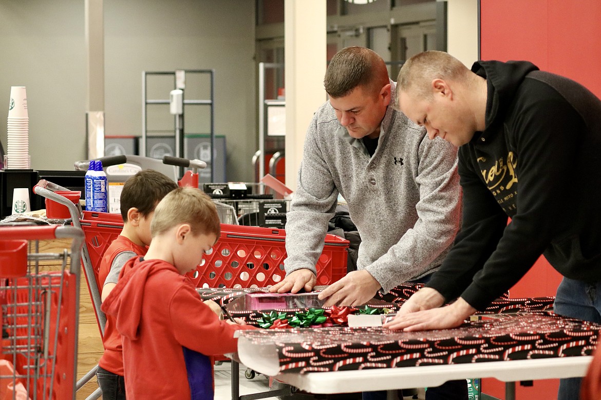 Six-year-old Giovanni and 5-year-old Logan (front) wrap gifts with the assistance of their military buddies First Sergeant Jim Pope (left) and First Sergeant Will Knapp at Target in Coeur d'Alene on Tuesday morning. HANNAH NEFF/Press