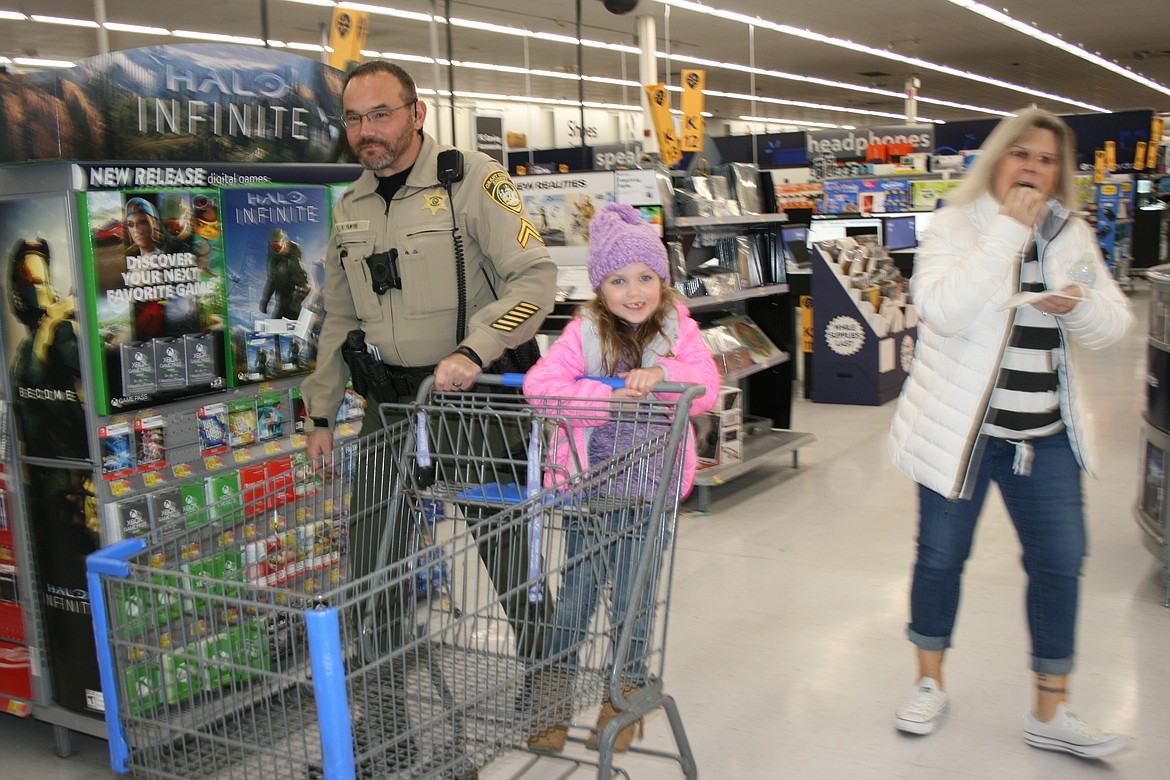 Grant County Sheriff’s Deputy Tom Tufte, left, takes Harmony Nichols for a ride on the shopping cart during Shop With A Cop.