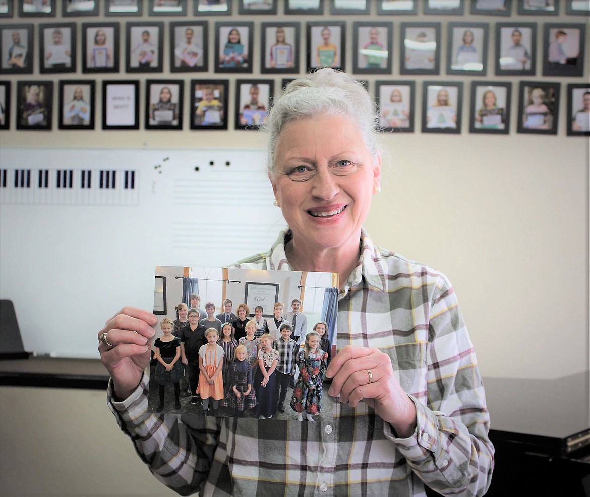 Glenda Novinger, who has been teaching music for almost 40 years, holds a picture of her students with pictures of other students behind her.