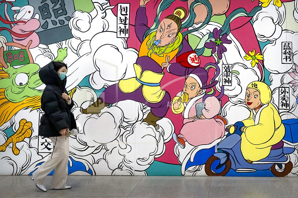 A woman wearing a face mask to protect against COVID-19 walks past a mural in the central business district in Beijing, Thursday, Dec. 23, 2021. China ordered the lockdown of as many as 13 million people in neighborhoods and workplaces in the northern city of Xi'an following a spike in coronavirus cases, setting off panic buying just weeks before the country hosts the Winter Olympic Games. (AP Photo/Mark Schiefelbein)