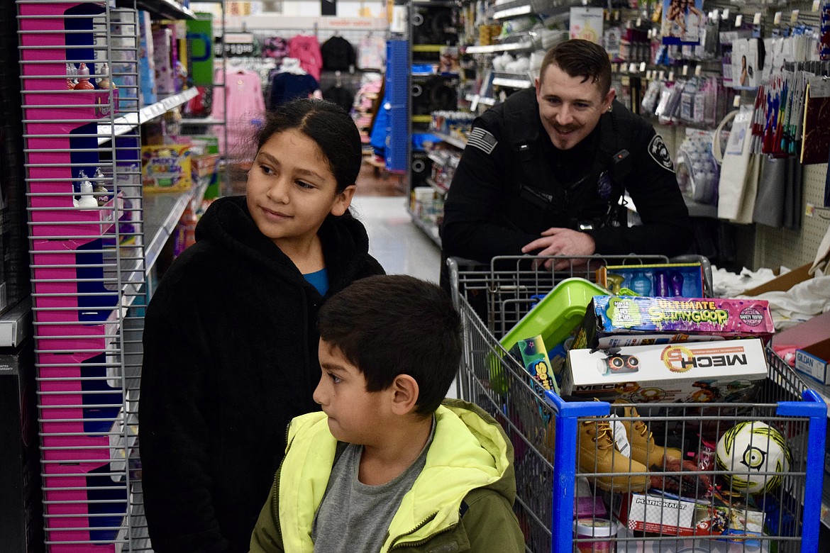 Zack Rodriguez, 6, front, and his sister Lidia Rodriguez, 9, look for presents, while Soap Lake Police Department Officer Jeff Gallaher pushes a cart at the SLPD’s Shop With A Cop on Thursday.