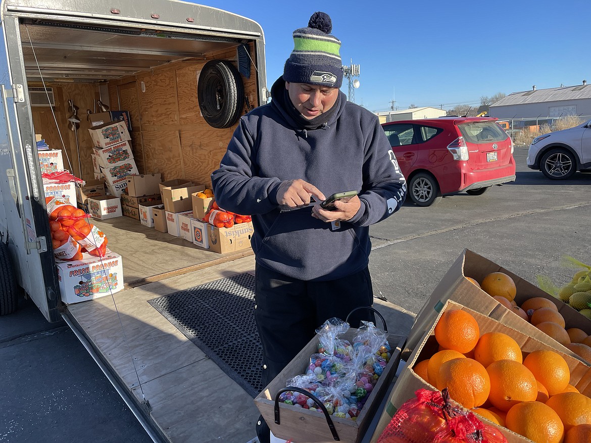 Produce seller Hernani Correia runs a customer’s debit card at the outdoor produce stand he runs in Moses Lake, where Correia was Monday despite temperatures below 15 degrees.