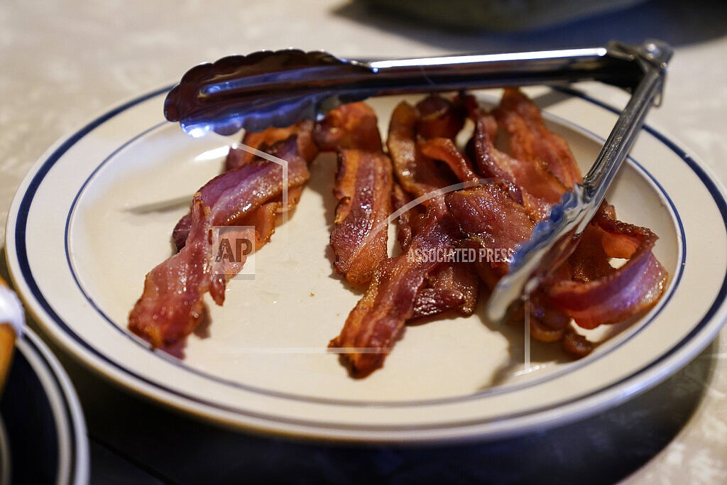 FILE - A plate of bacon sits on the kitchen table on the Ron Mardesen farm, Thursday, Dec. 2, 2021, near Elliott, Iowa. A 2018 voter-approved California ballot measure, to take effect, Jan. 1, 2022, set the nation's toughest living space standards for breeding pigs. Critics have called for putting off enforcement until 2024 for fear prices will rise and jobs will be lost. Mardesen already meets the California standards for the hogs he sells to specialty meat company Niman Ranch, which supported passage of Proposition 12 and requires all of its roughly 650 hog farmers to give breeding pigs far more room than mandated by the law. (AP Photo/Charlie Neibergall,File)