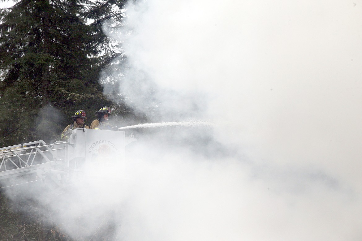 Firefighters spray water on a home on fire on East Fernan Lake Road on March 25.