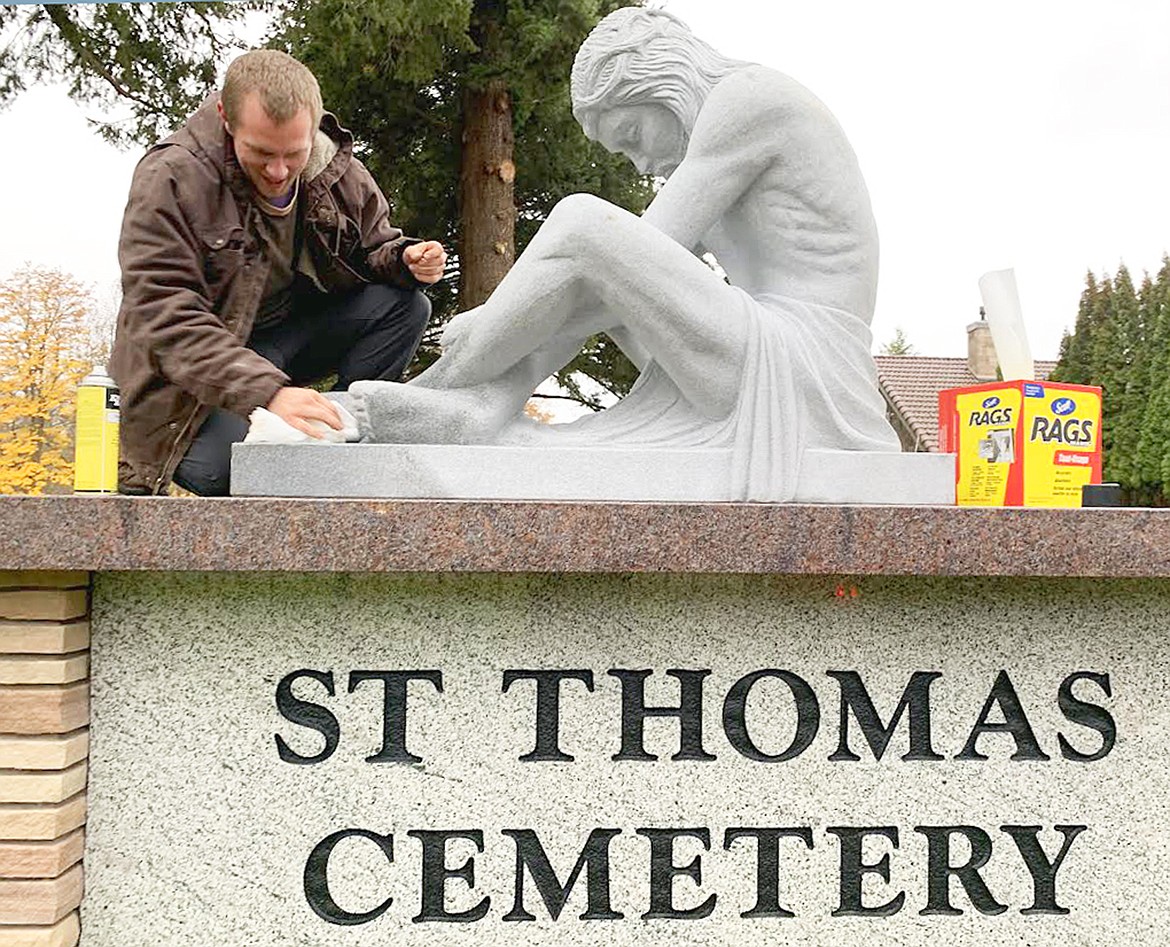 Brandon Mitchell with Memorial Monuments cleans the feet of the statue of Jesus Christ that was put in place on top of a sign in the northwest corner of St. Thomas Cemetery in late October. The $17,000, granite statue was paid for by an anonymous donor.