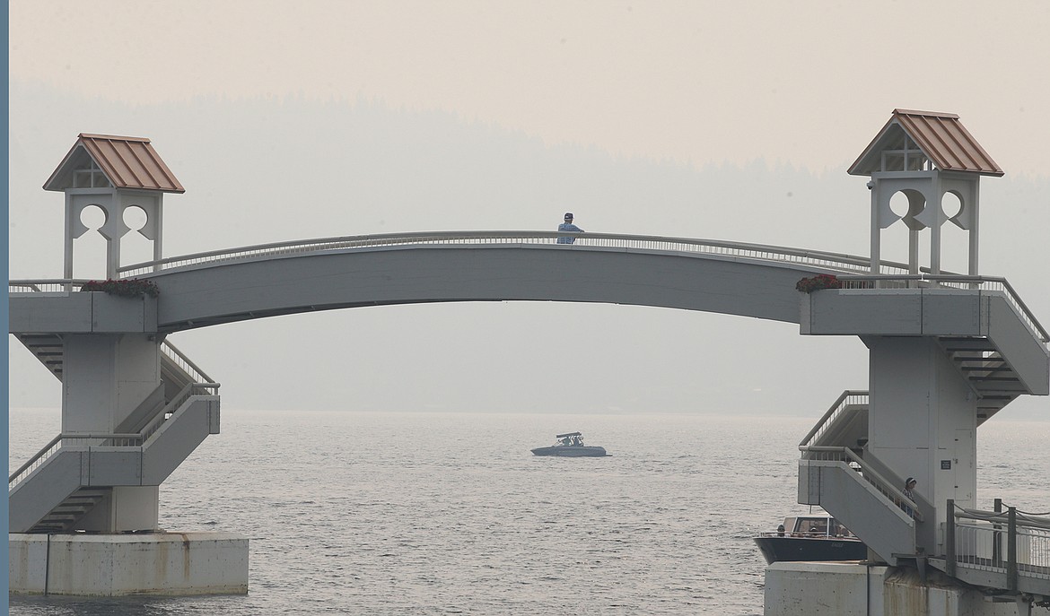 A man standing on The Boardwalk bridge at The Coeur d'Alene Resort looks through the smoky haze as a boat passes by in the distance on Aug. 2.