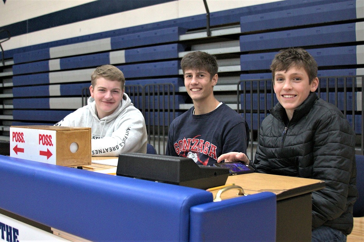 Boys varsity basketball players Trey Bateman, Riley Petesch and Asher Williams man the score board and take stats at the Alumni tournament.