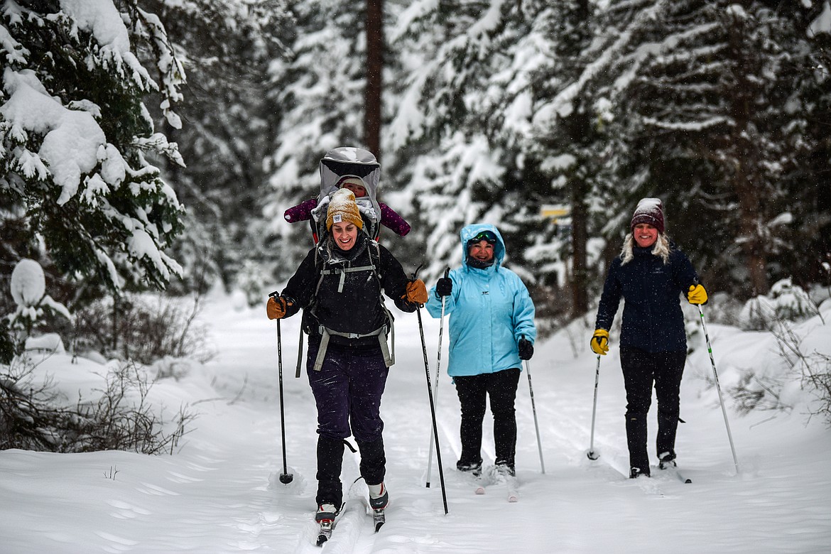 From left, Kali Tholen with 9-month-old Ila on her back, Amy Schmidt and Mattie Willette cross-country ski along the Aeneas Loop at the Bigfork Community Nordic Center trails on Foothill Road on Thursday, Jan. 6. (Casey Kreider/Daily Inter Lake)