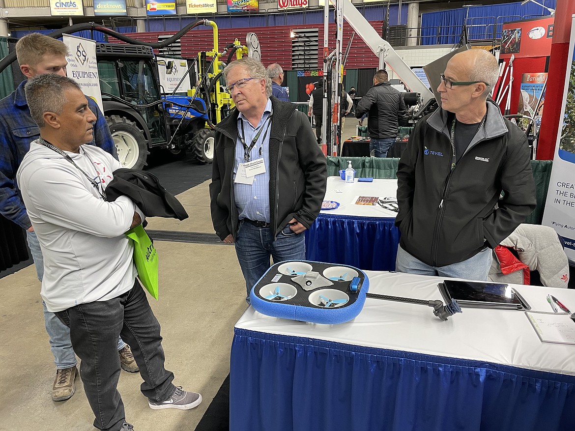 Tevel Aerobotics Technologies board chair Eyal Desheh (center) and engineer David Vita (right) talk with an orchard supervisor about how quickly their equipment harvests apples.