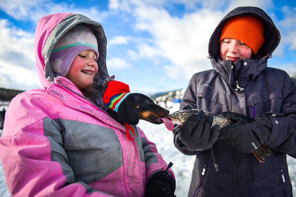 Alina Johnson, left, keeps her family's mini dachshund named Coco warm inside her jacket while it gives a kiss to a pike caught by her sister Alona at the 51st Sunriser Lions Family Ice Fishing Derby at Smith Lake in Kila on Saturday, Jan. 8. (Casey Kreider/Daily Inter Lake)